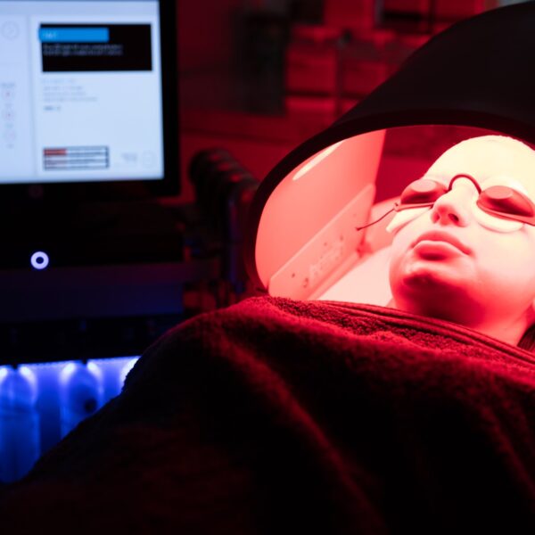 A patient reclined under a red LED phototherapy panel in the Regents Park Aesthetics treatment room